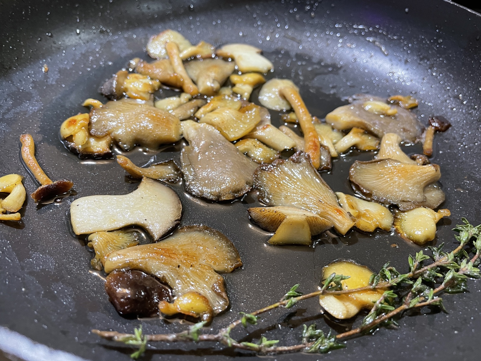 Home-grown gourmet mushrooms searing golden in a pan with fresh thyme